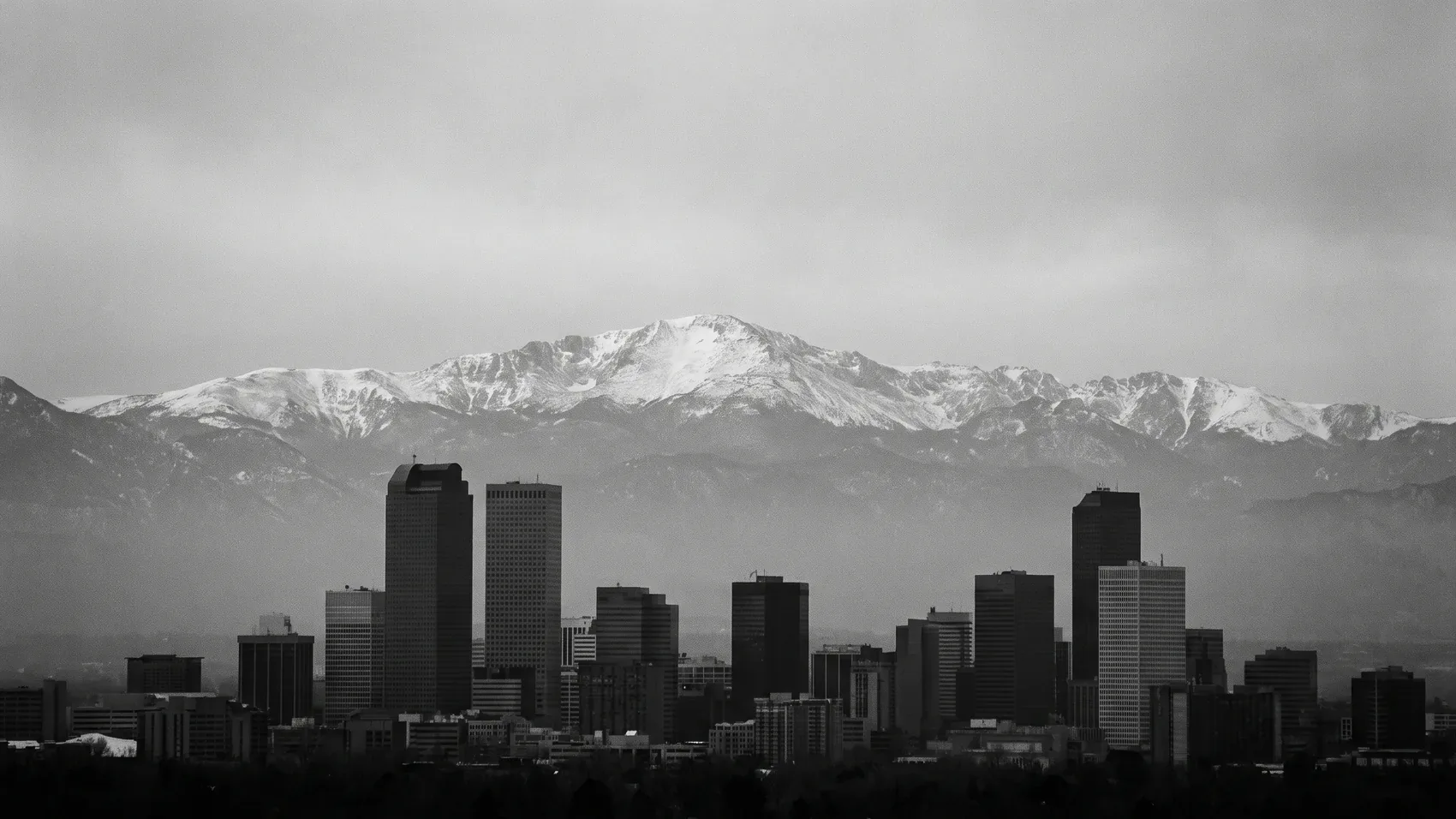 The Denver skyline with the Rocky Mountains behind it, in black and white.
